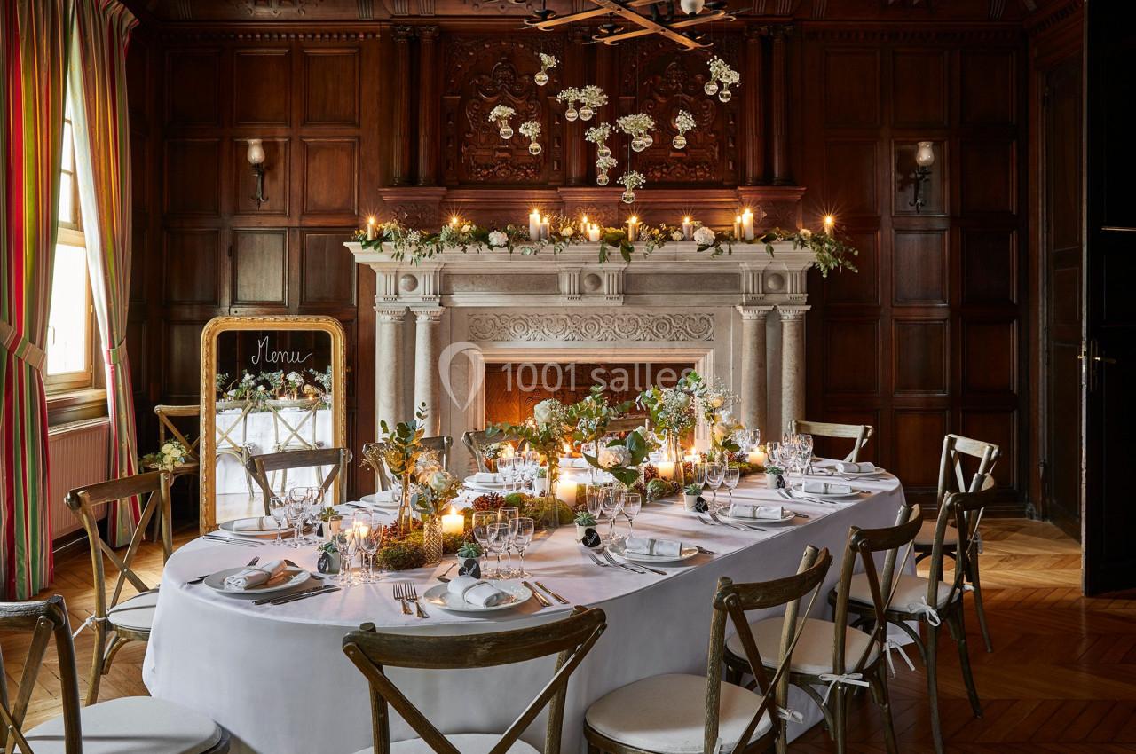 Table élégamment dressée dans une salle en bois avec cheminée ornée de fleurs et bougies allumées.