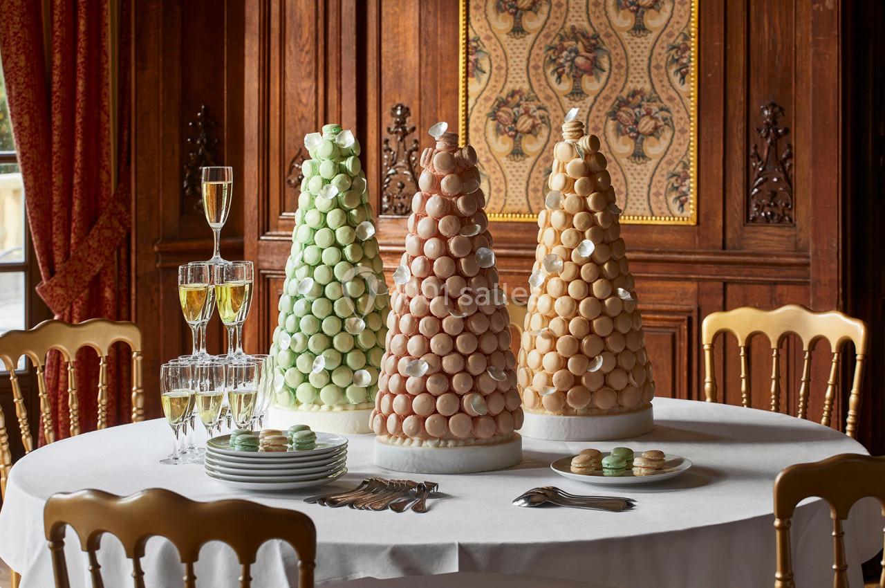 Trois pyramides de macarons colorés sur une table dressée avec couverts, assiettes et flûtes de champagne dans une salle…