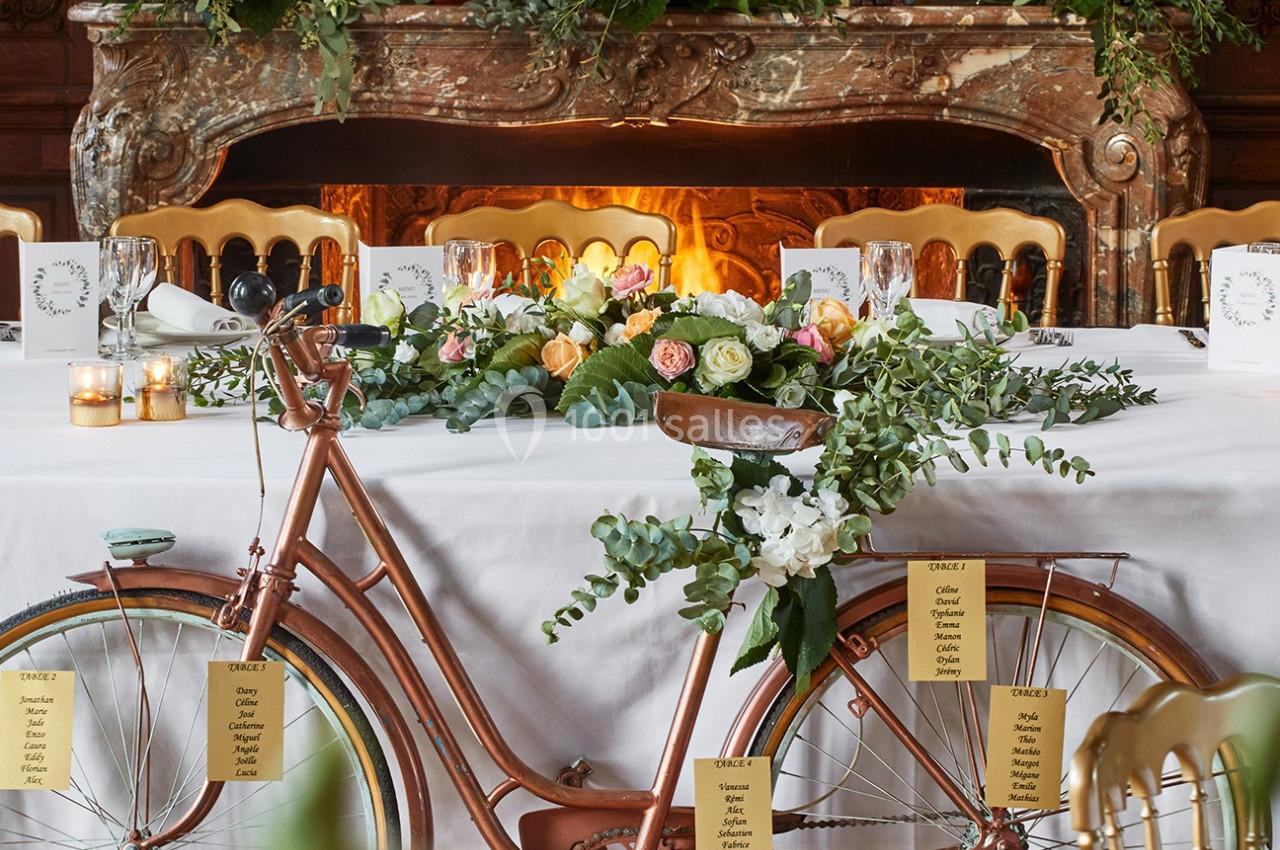 Vélo décoratif en métal cuivré orné de fleurs et de feuillage, placé devant une table de réception élégante.