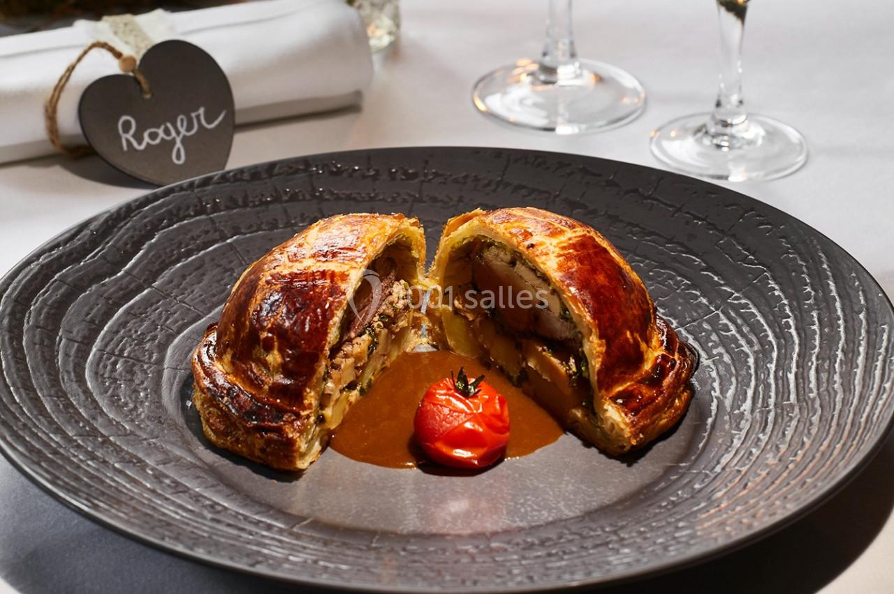 Plat de viande en croûte servi avec une sauce, une tomate rôtie et une présentation soignée sur une assiette sombre.