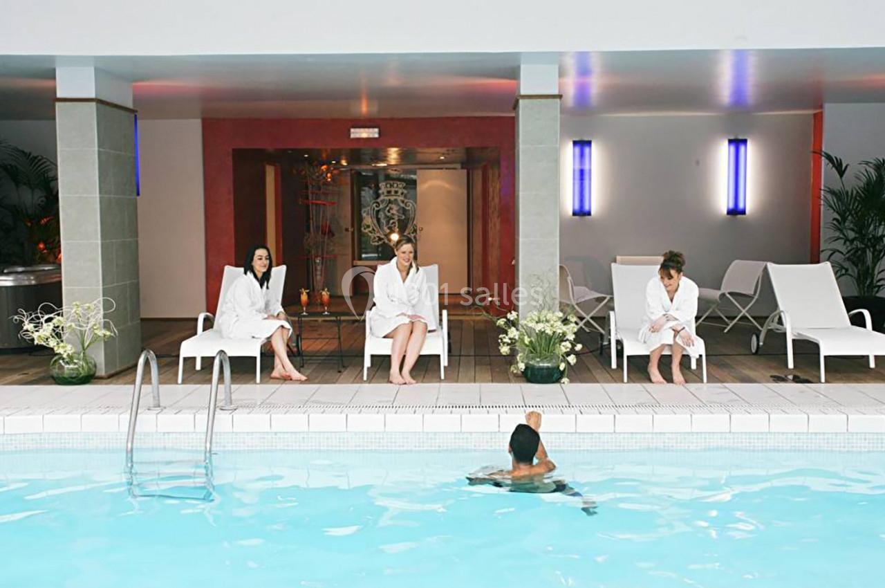 Des personnes en peignoirs assises sur des chaises longues près d'une piscine intérieure, avec une personne dans l'eau.