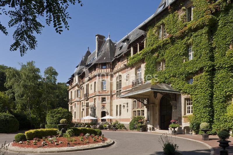 Façade d'un bâtiment ancien recouvert de lierre, entouré de jardins bien entretenus et d'arbres.