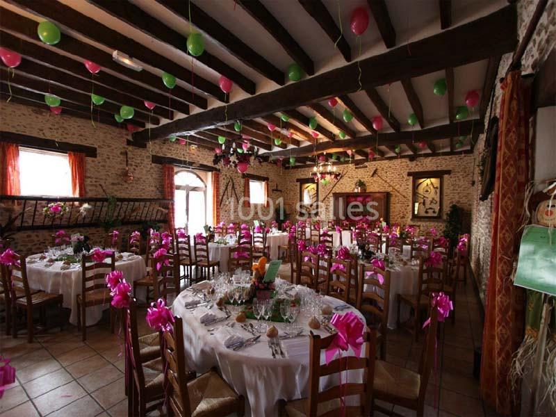 Salle de réception décorée avec des ballons et des rubans roses, tables rondes dressées pour un événement festif.