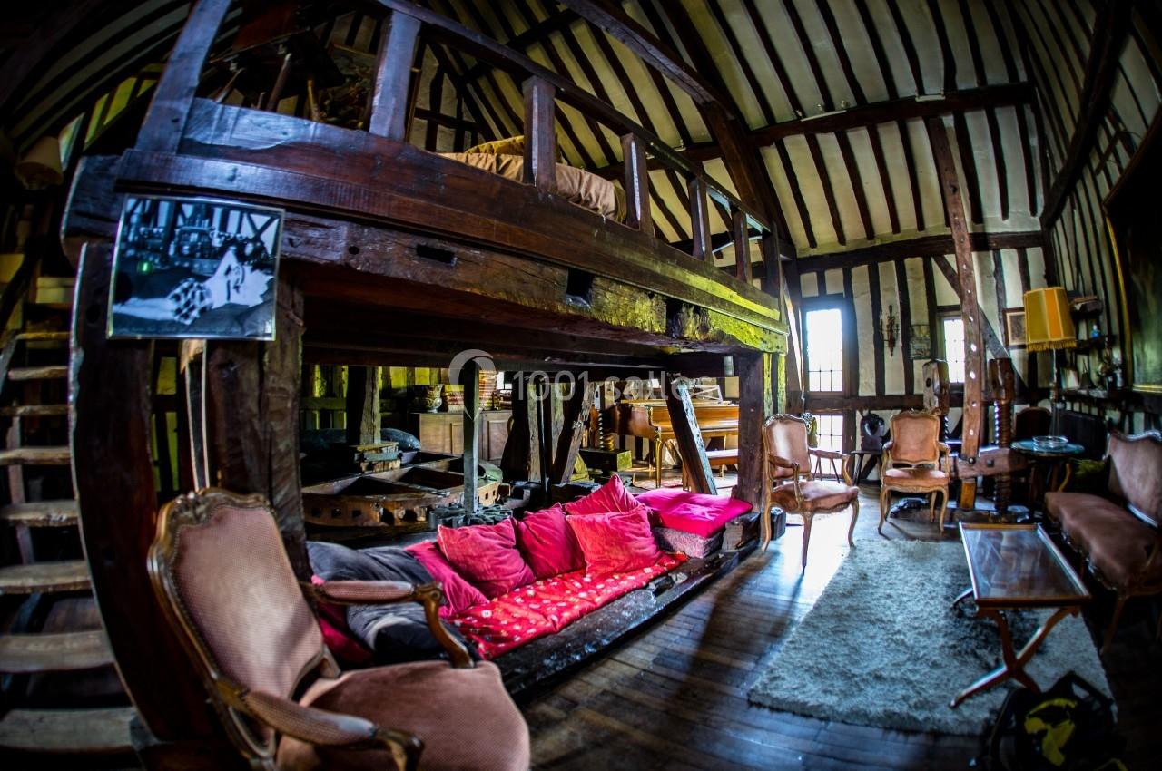 Salon rustique avec poutres apparentes, mezzanine en bois, canapé avec coussins colorés et meubles anciens.