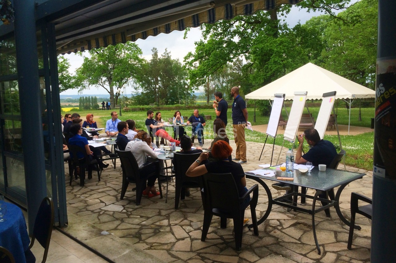 Un groupe de personnes participe à une réunion en plein air sous une tente, avec des tableaux de présentation.