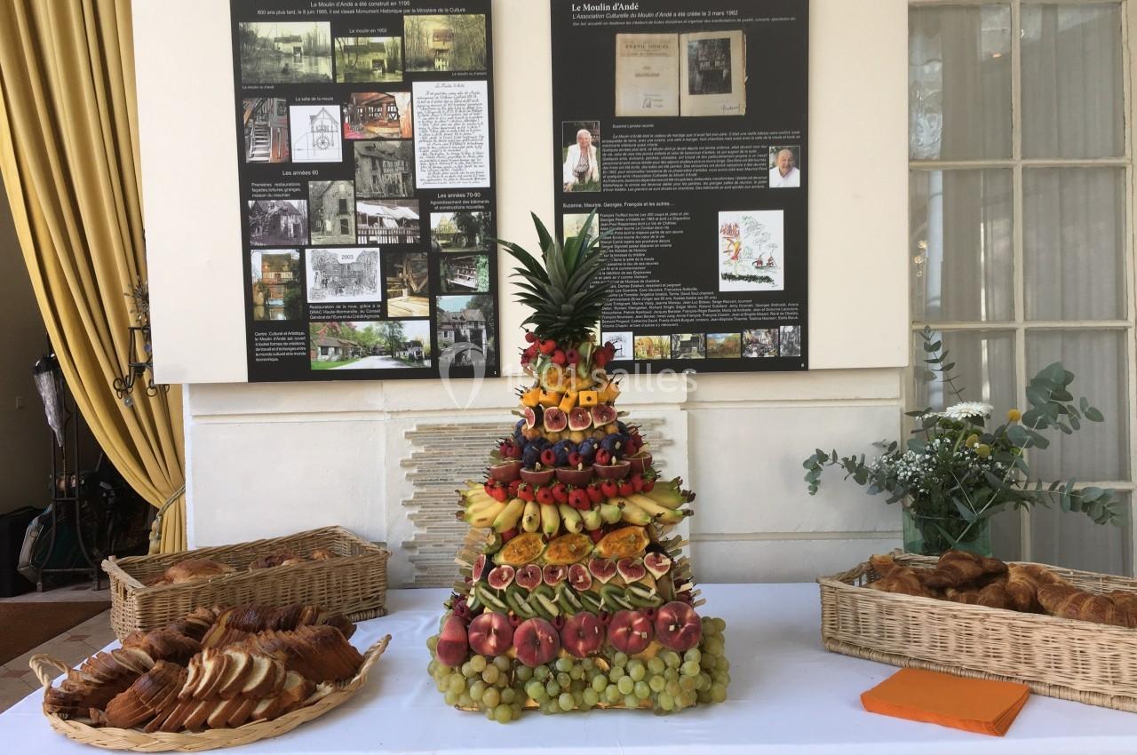 Présentation d'un buffet avec une pyramide de fruits, des viennoiseries et des tranches de pain, devant des panneaux d…