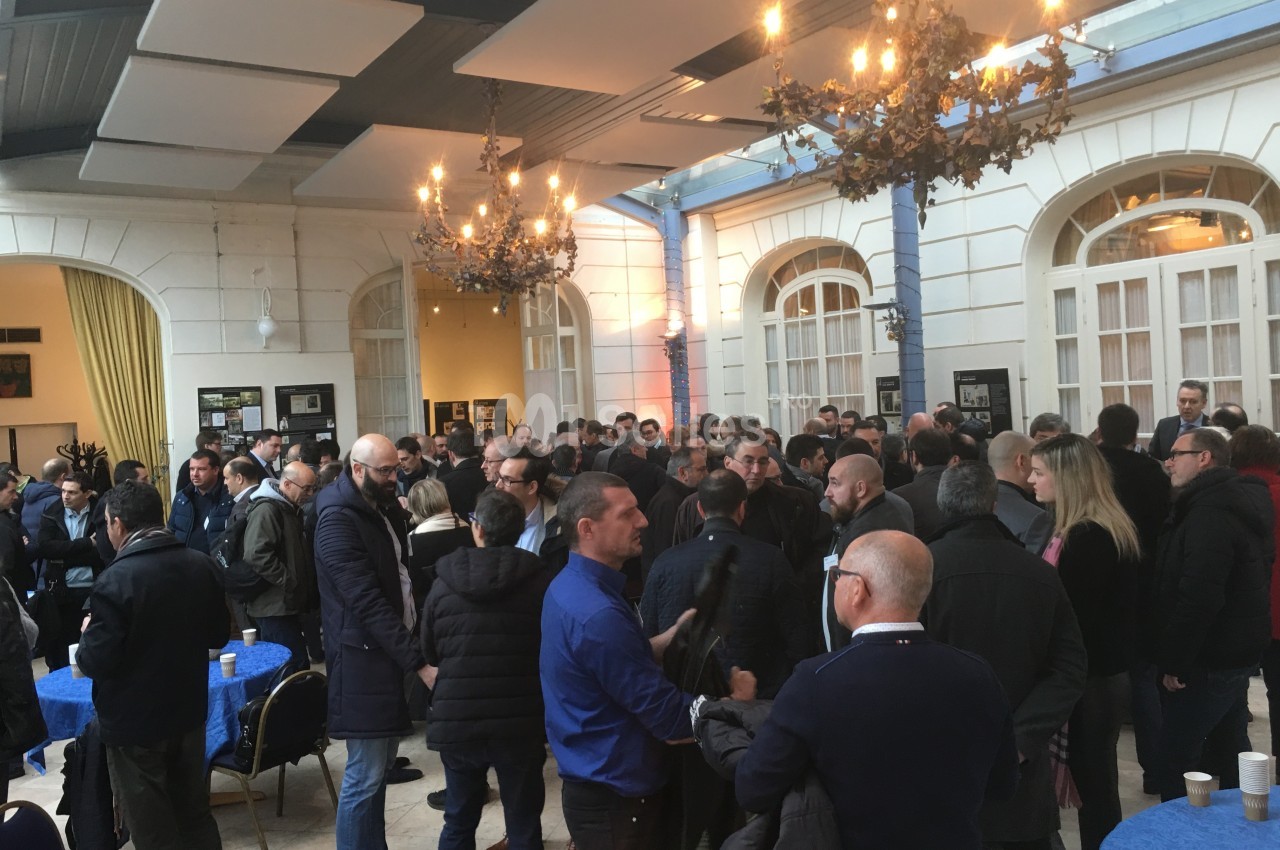 Groupe de personnes discutant dans une salle lumineuse avec des lustres et des tables rondes bleues.