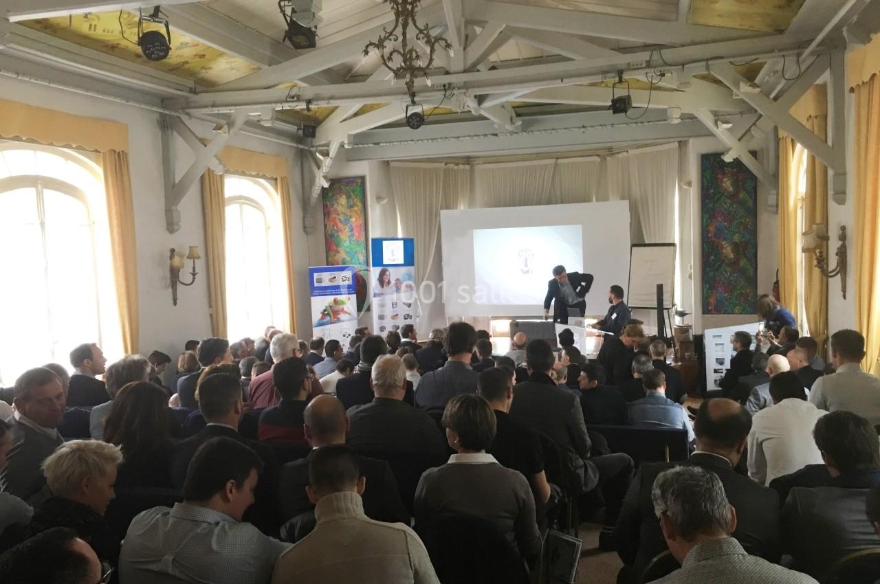 Salle de conférence remplie de participants assis, regardant une présentation projetée sur un écran.