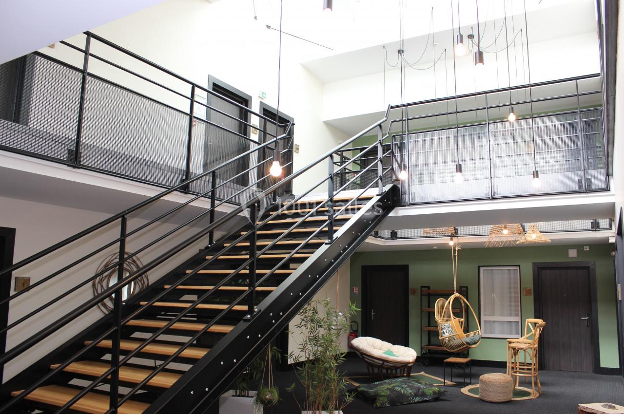 Escalier métallique moderne dans un espace intérieur lumineux avec mobilier en rotin et plantes décoratives.