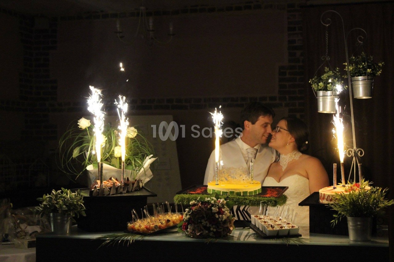 Un couple de mariés se tient près d'une table décorée avec des desserts et des fontaines lumineuses allumées.