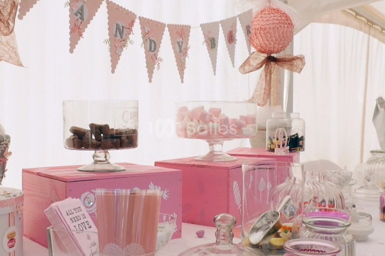Table décorée avec des bonbonnières remplies de sucreries, des boîtes roses et une guirlande festive en arrière-plan.