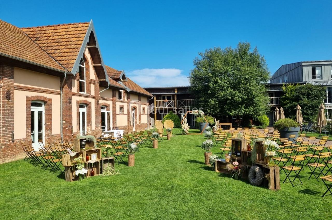 Jardin aménagé pour un événement avec chaises, décorations rustiques en bois et bâtiment en briques en arrière-plan.