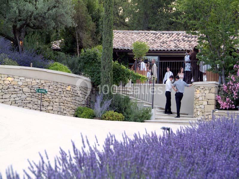 Location salle Sorgues (Vaucluse) - Château La Tour Vaucros #6 Maison en pierre entourée de lavande et de végétation, avec des personnes discutant près d'une terrasse.