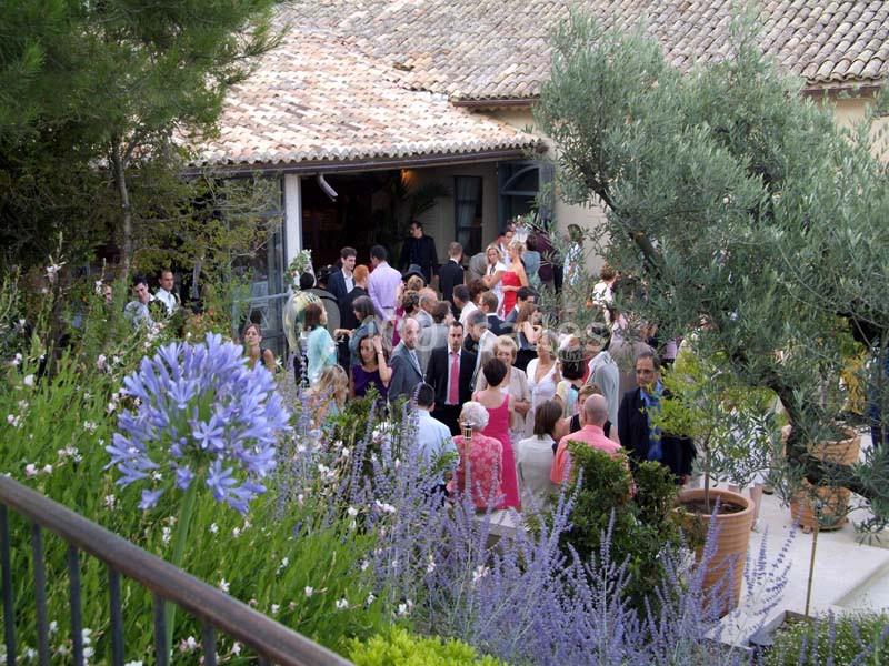 Location salle Sorgues (Vaucluse) - Château La Tour Vaucros #8 Groupe de personnes rassemblées dans un jardin fleuri près d'une maison au toit de tuiles.
