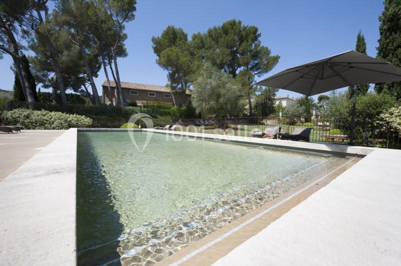 Location salle Sorgues (Vaucluse) - Château La Tour Vaucros #2 Piscine extérieure entourée de végétation, avec parasol, transats et maisons en arrière-plan sous un ciel dégagé.