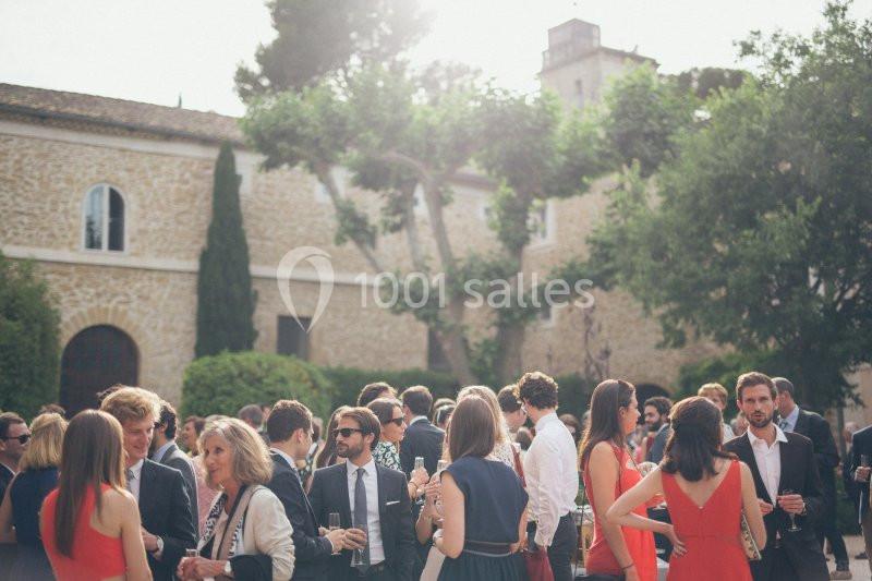 Location salle Sorgues (Vaucluse) - Château La Tour Vaucros #5 Groupe de personnes en tenue élégante discutant dans une cour extérieure bordée d'arbres et de bâtiments en pierre.