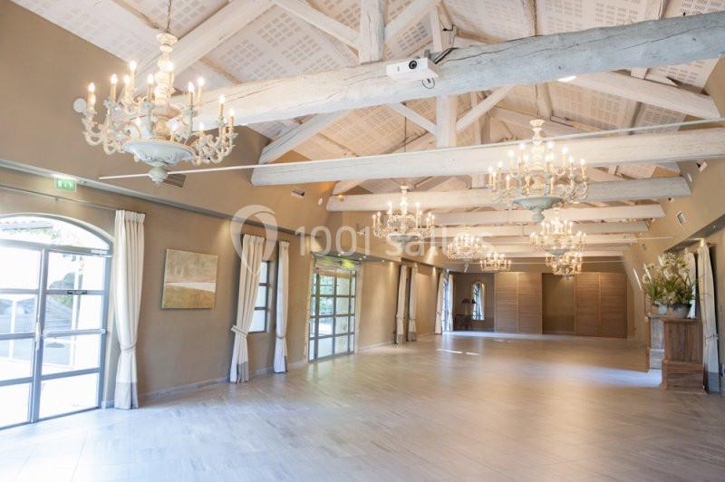 Location salle Sorgues (Vaucluse) - Château La Tour Vaucros #9 Salle lumineuse avec poutres apparentes, lustres suspendus, grandes fenêtres et sol en carrelage clair.