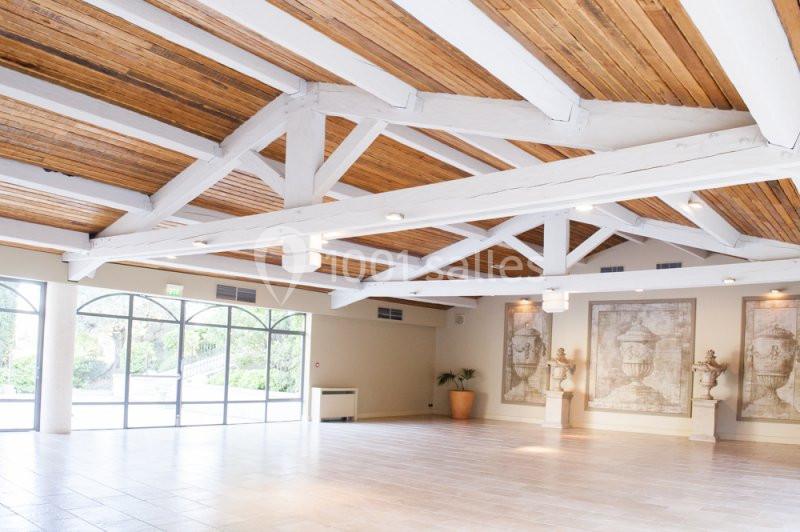 Location salle Sorgues (Vaucluse) - Château La Tour Vaucros #13 Salle lumineuse avec poutres apparentes en bois, grandes baies vitrées et murs décorés de tableaux classiques.