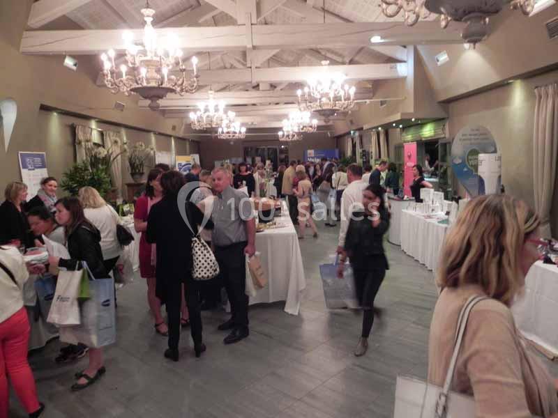 Location salle Sorgues (Vaucluse) - Château La Tour Vaucros #11 Des personnes discutent et explorent des stands dans une salle éclairée avec des lustres et des tables exposant des produits.