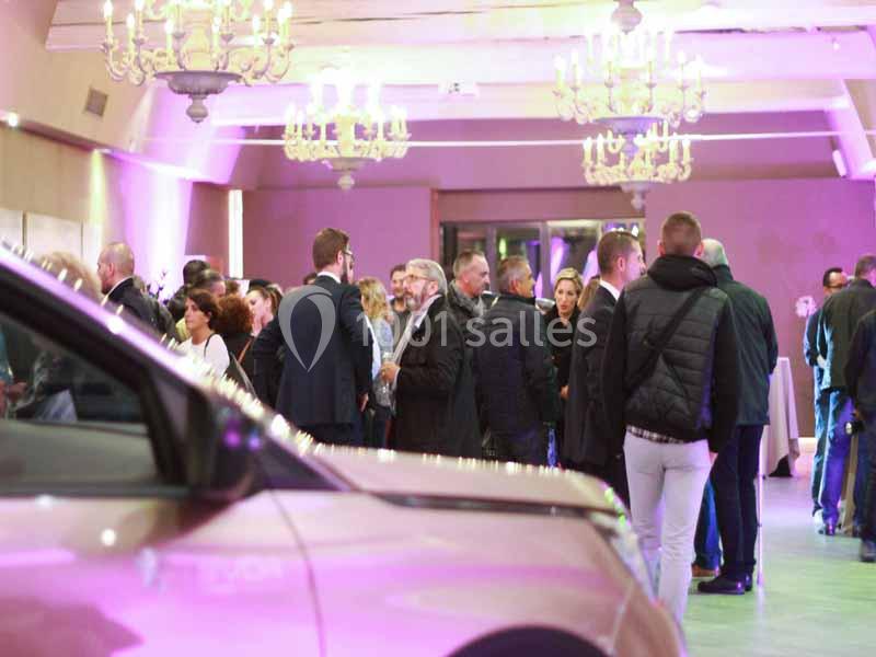 Location salle Sorgues (Vaucluse) - Château La Tour Vaucros #12 Groupe de personnes discutant dans une salle éclairée par des lustres, avec une voiture visible au premier plan.