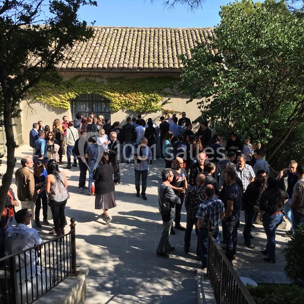 Location salle Sorgues (Vaucluse) - Château La Tour Vaucros #7 Groupe de personnes rassemblées en extérieur devant un bâtiment avec toit en tuiles, entouré de végétation.