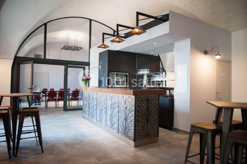 Location salle Sorgues (Vaucluse) - Château La Tour Vaucros #16 Salle moderne avec comptoir en métal décoratif, tabourets hauts, éclairage suspendu et vue sur une salle de réunion vitrée.