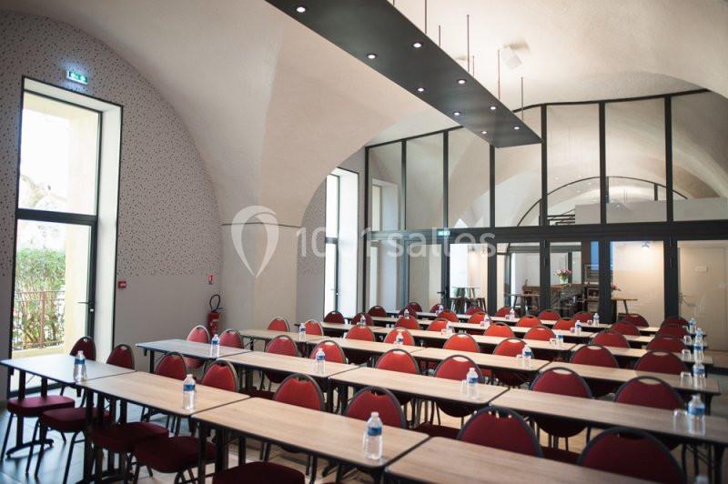 Location salle Sorgues (Vaucluse) - Château La Tour Vaucros #19 Salle de conférence lumineuse avec des tables alignées, des chaises rouges et une grande baie vitrée en arrière-plan.