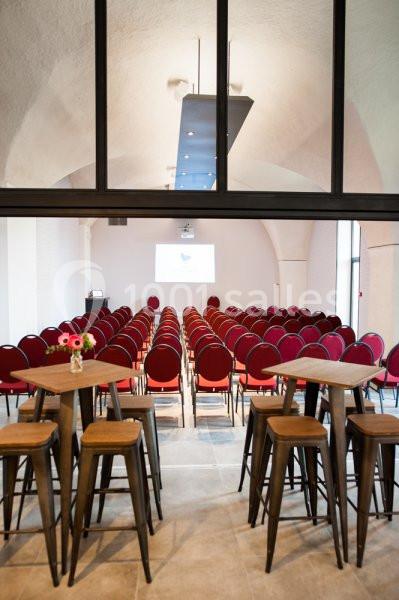 Location salle Sorgues (Vaucluse) - Château La Tour Vaucros #21 Salle de conférence avec rangées de chaises rouges alignées, écran de projection et tables hautes au premier plan.