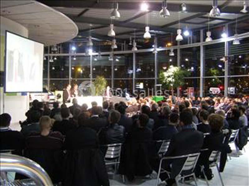 Salle remplie de personnes assistant à une présentation projetée sur un écran dans un espace moderne et éclairé.