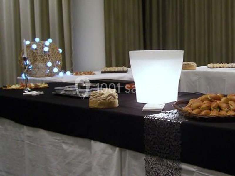 Table de buffet avec nappes noires et blanches, contenant des plats variés et une lampe décorative allumée.