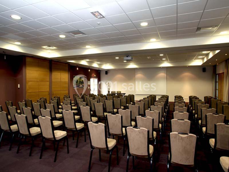 Salle de conférence vide avec rangées de chaises alignées face à un écran blanc et un projecteur au plafond.