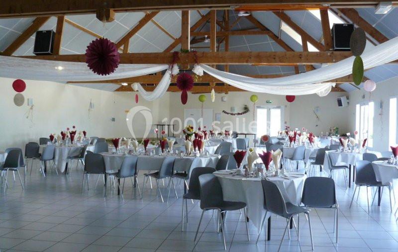 Salle de réception décorée avec des tables rondes dressées, nappes blanches, chaises grises et suspensions colorées.
