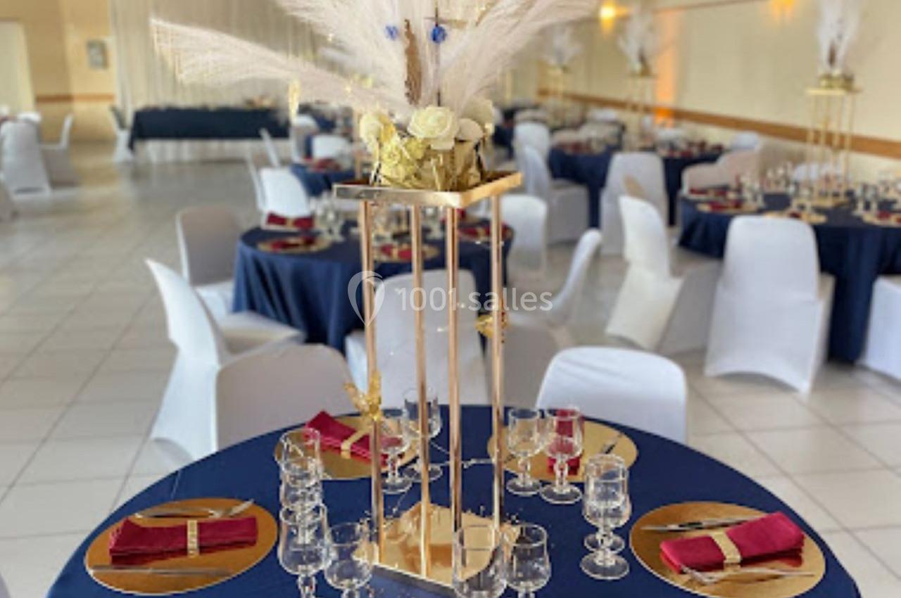 Salle de réception décorée avec des tables rondes, nappes bleues, serviettes rouges et centre de table floral élégant.