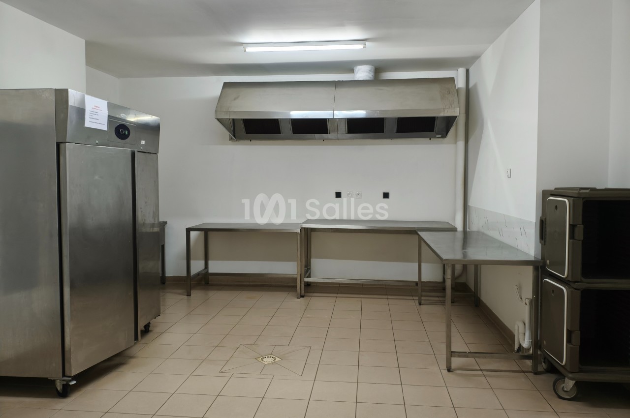 Cuisine professionnelle vide avec sol carrelé, plans de travail en inox, hotte aspirante et équipements de rangement.