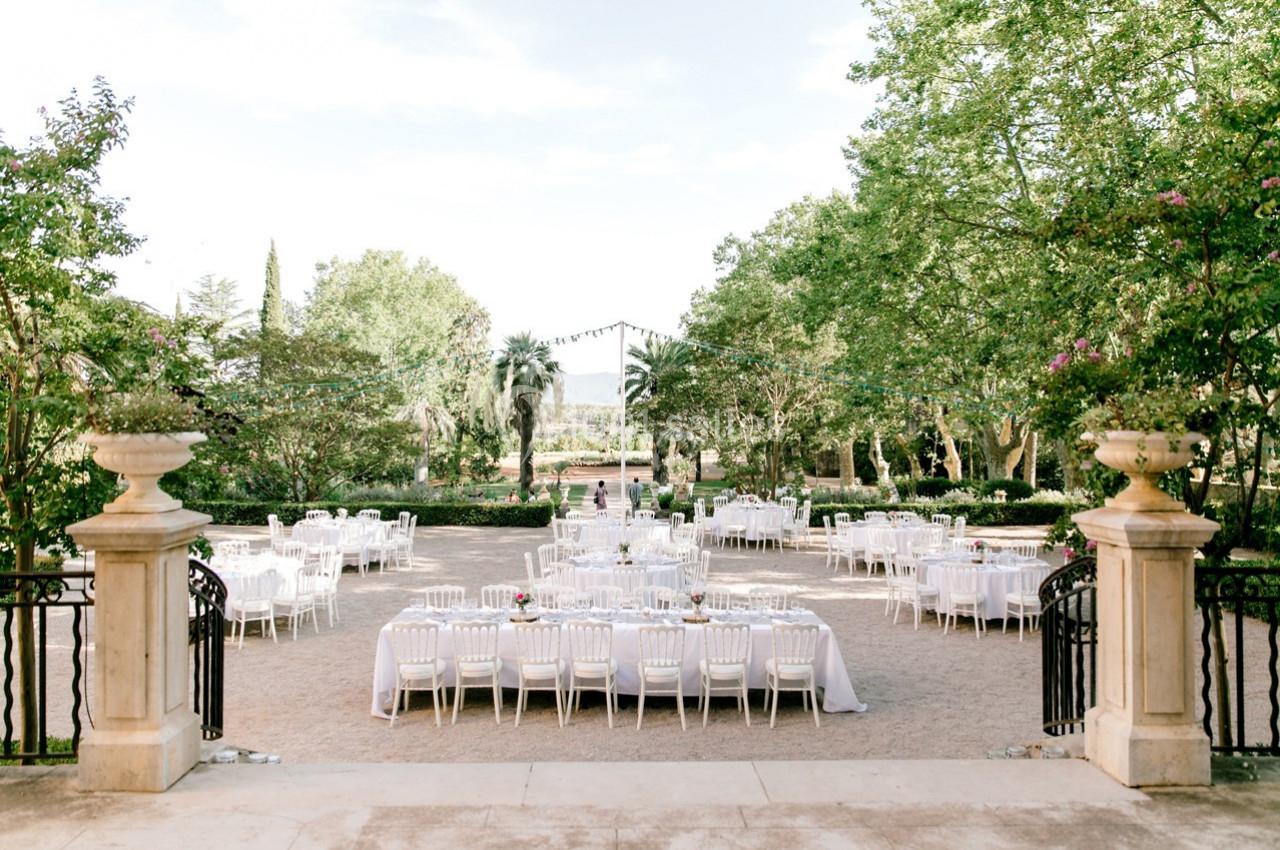 Location salle Le Cannet-des-Maures (Var) - Château Colbert Cannet #7 Tables dressées pour un événement en plein air dans un jardin avec des arbres et des guirlandes lumineuses.