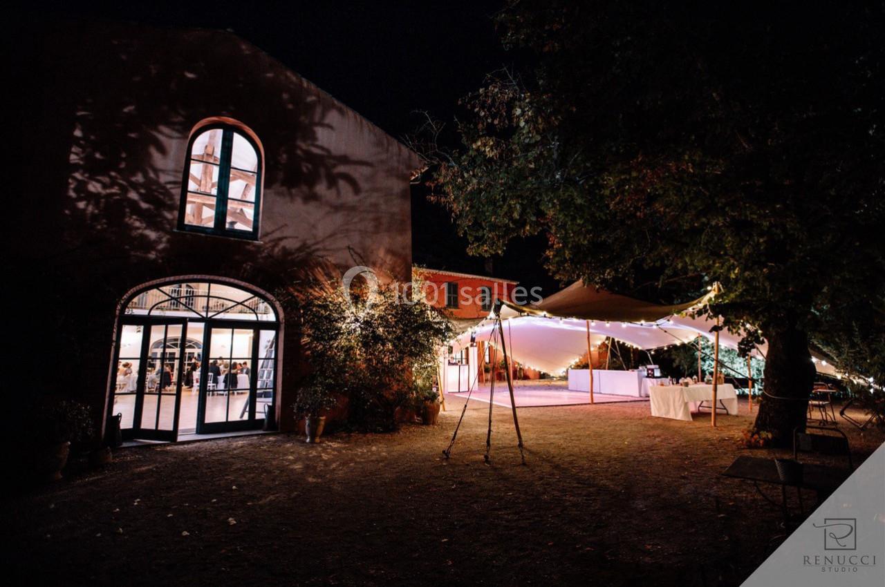 Location salle Le Cannet-des-Maures (Var) - Château Colbert Cannet #15 Bâtiment en pierre éclairé de nuit avec une tente lumineuse installée dans un jardin adjacent.
