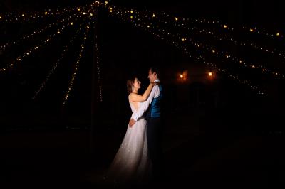 Miniature Location salle Le Cannet-des-Maures (Var) - Château Colbert Cannet #9 Un couple danse sous des guirlandes lumineuses devant un bâtiment éclairé en rouge, de nuit.