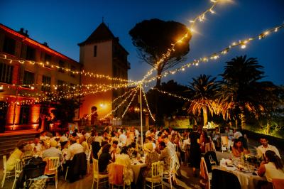 Miniature Location salle Le Cannet-des-Maures (Var) - Château Colbert Cannet #11 Un couple danse sous des guirlandes lumineuses devant un bâtiment éclairé en rouge, de nuit.