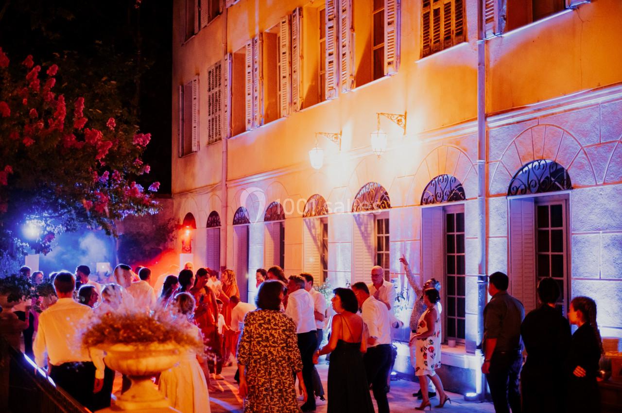 Location salle Le Cannet-des-Maures (Var) - Château Colbert Cannet #10 Groupe de personnes dansant en soirée devant un bâtiment éclairé par des lumières colorées.