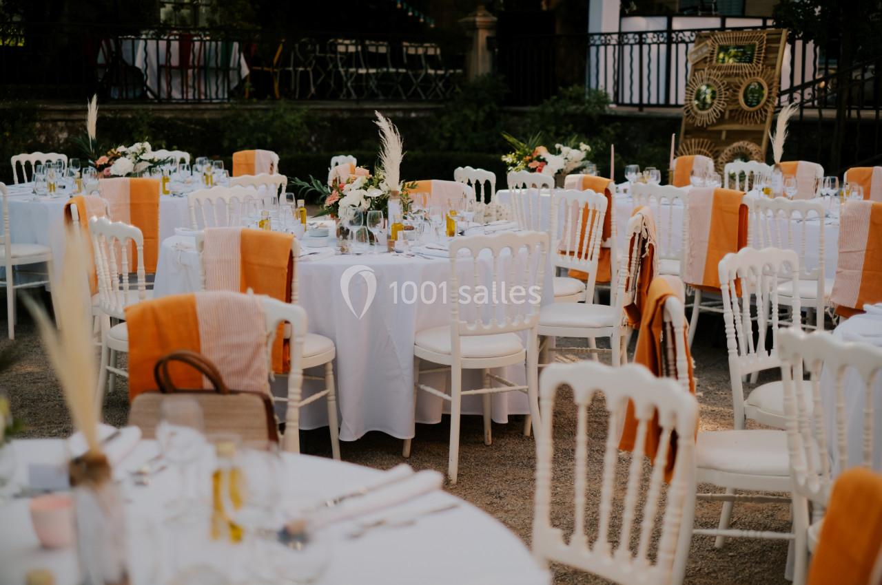 Location salle Le Cannet-des-Maures (Var) - Château Colbert Cannet #6 Tables rondes décorées de nappes blanches et chaises blanches avec des touches orange, disposées en extérieur.