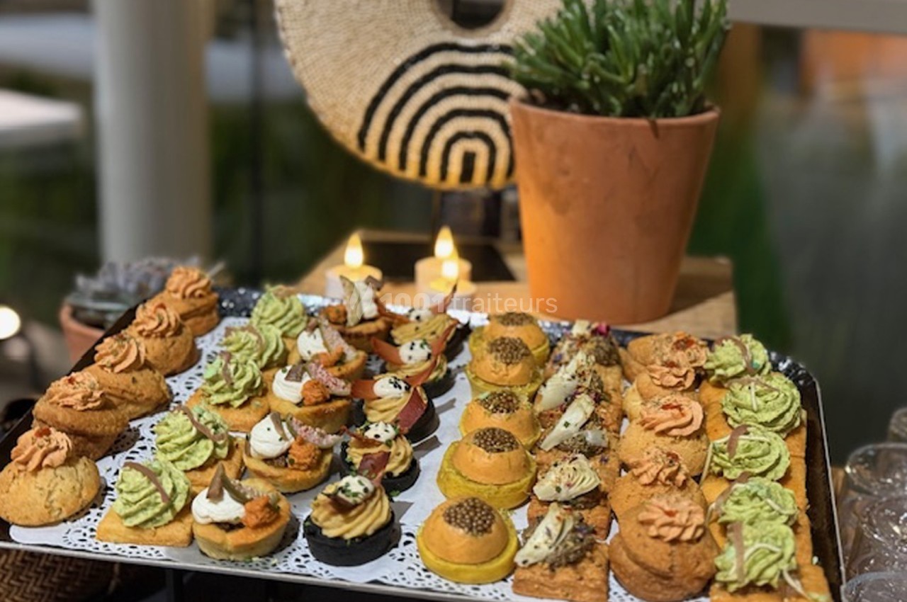 Plateau de bouchées salées variées avec garnitures colorées, présenté sur une table décorée de plantes et bougies.