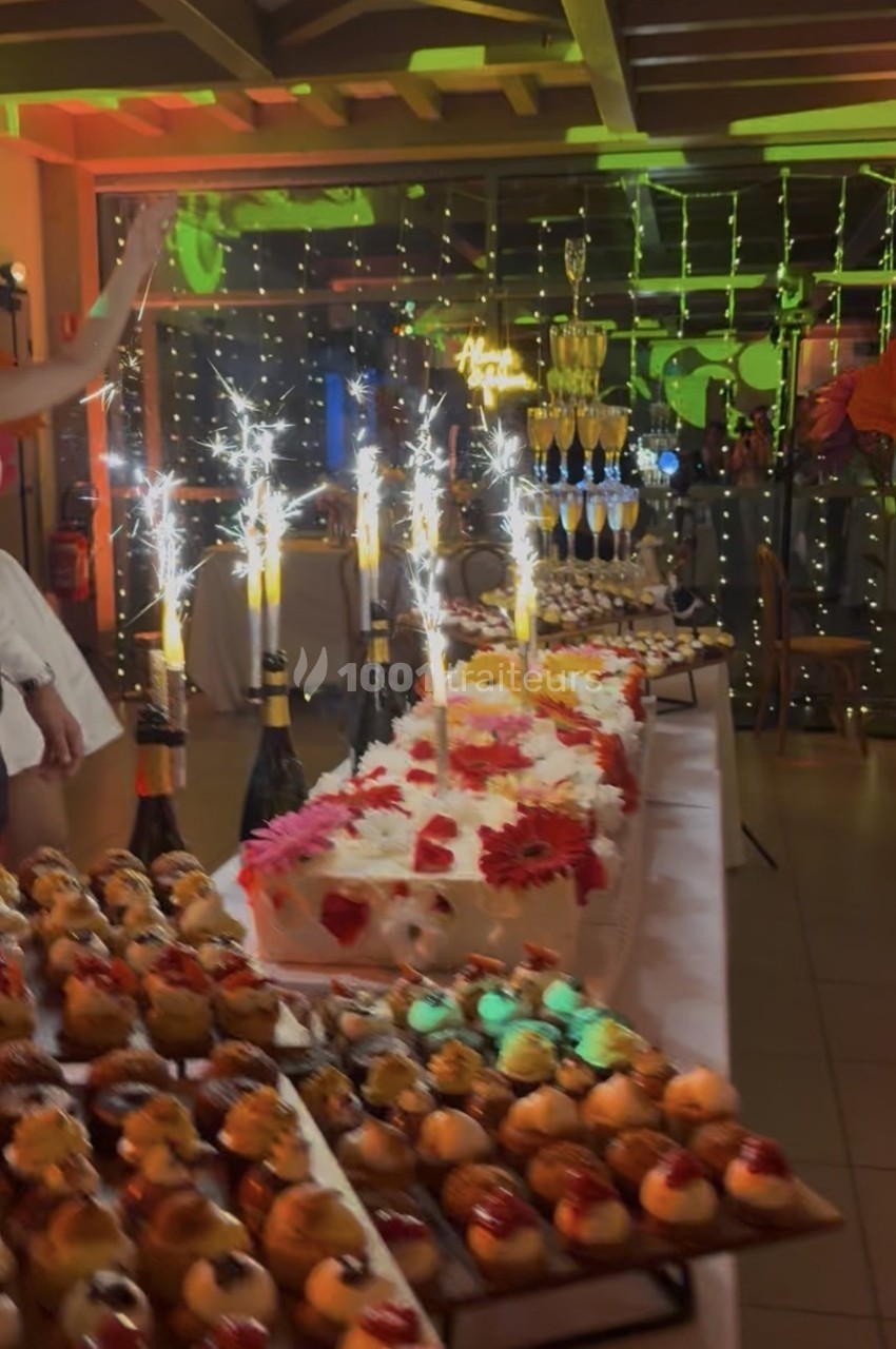 Table de desserts décorée avec des gâteaux, des fontaines lumineuses et une pyramide de coupes de champagne en arrière-plan.