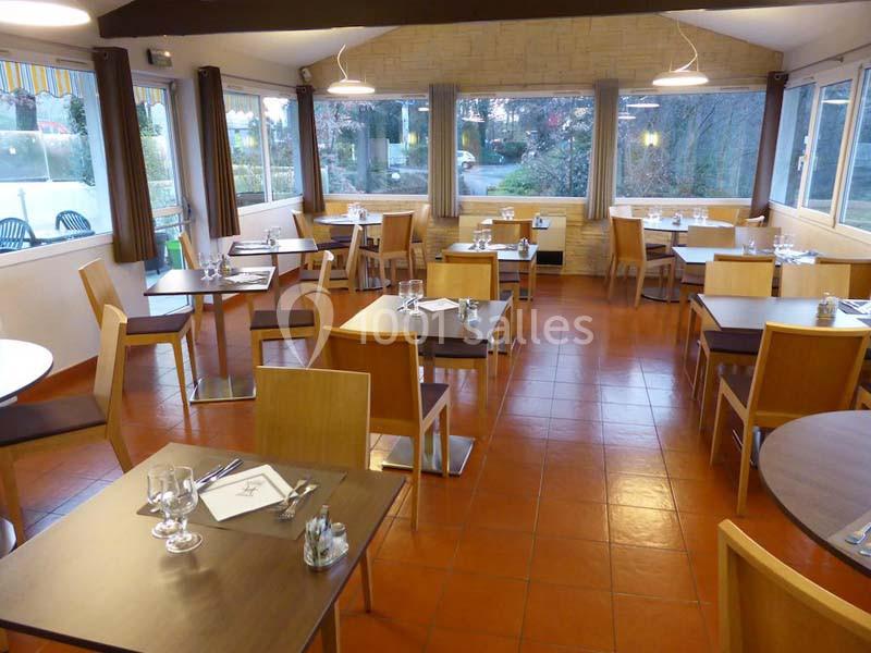 Salle de restaurant lumineuse avec tables en bois dressées, grandes fenêtres donnant sur un jardin.