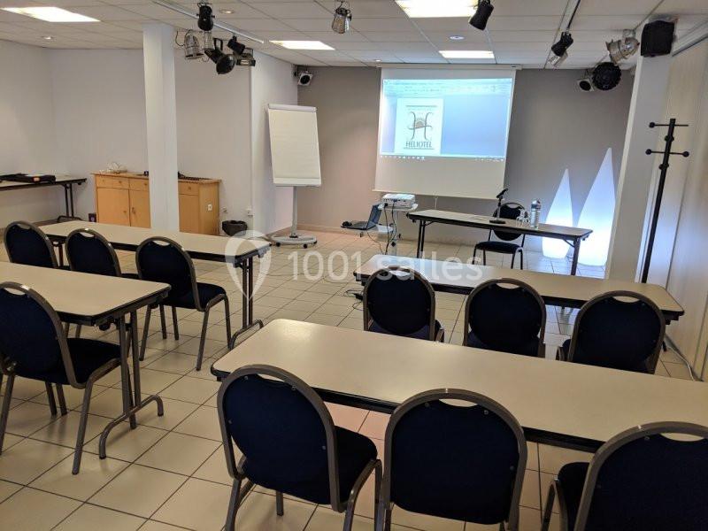 Salle de réunion équipée de tables, chaises, tableau blanc, projecteur et écran, prête pour une présentation.