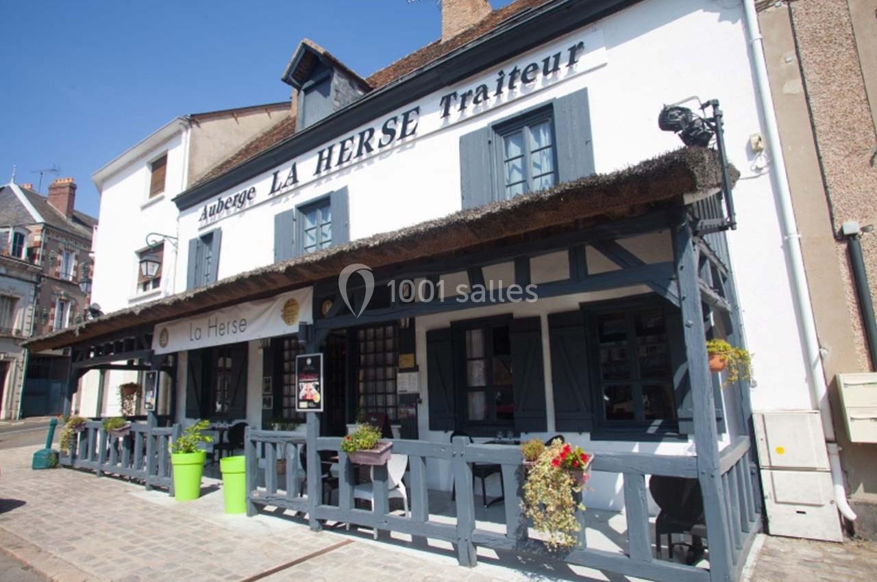 Façade d'une auberge traditionnelle avec terrasse en bois, pots de fleurs et enseigne visible dans une rue calme.