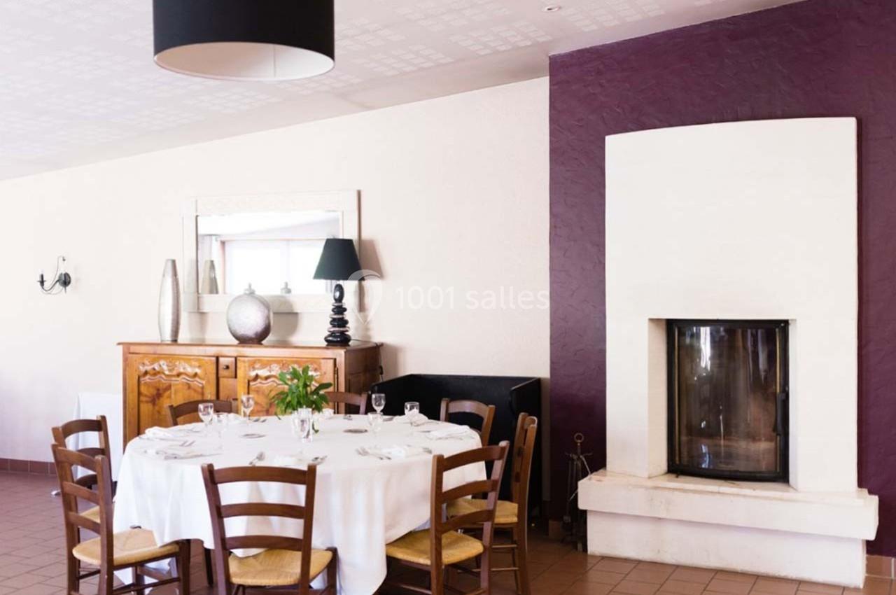 Location salle Bonneval (Eure-et-Loir) - Auberge de La Herse #4 Salle à manger avec table ronde dressée, cheminée moderne, buffet en bois et mur violet en arrière-plan.