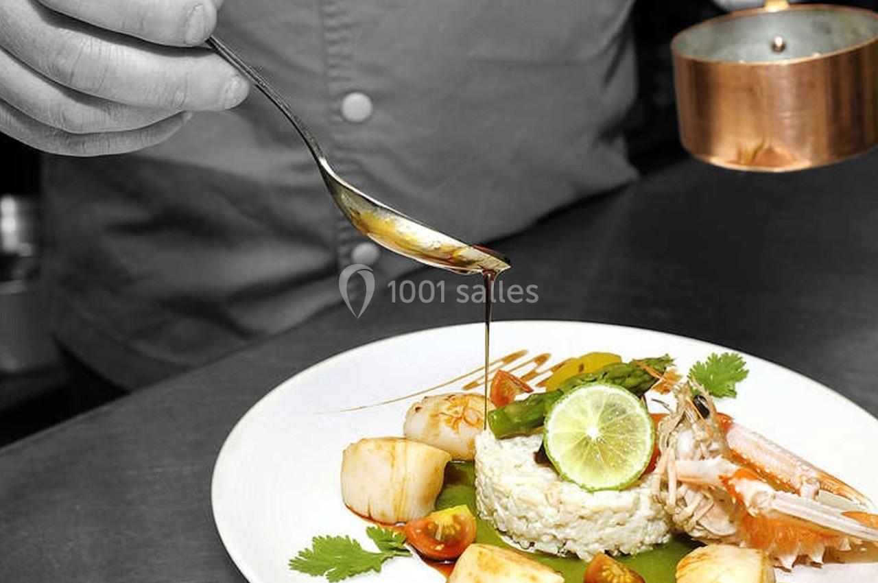 Location salle Bonneval (Eure-et-Loir) - Auberge de La Herse #6 Un chef verse une sauce sur un plat composé de riz, noix de Saint-Jacques, crevette, légumes et citron vert.