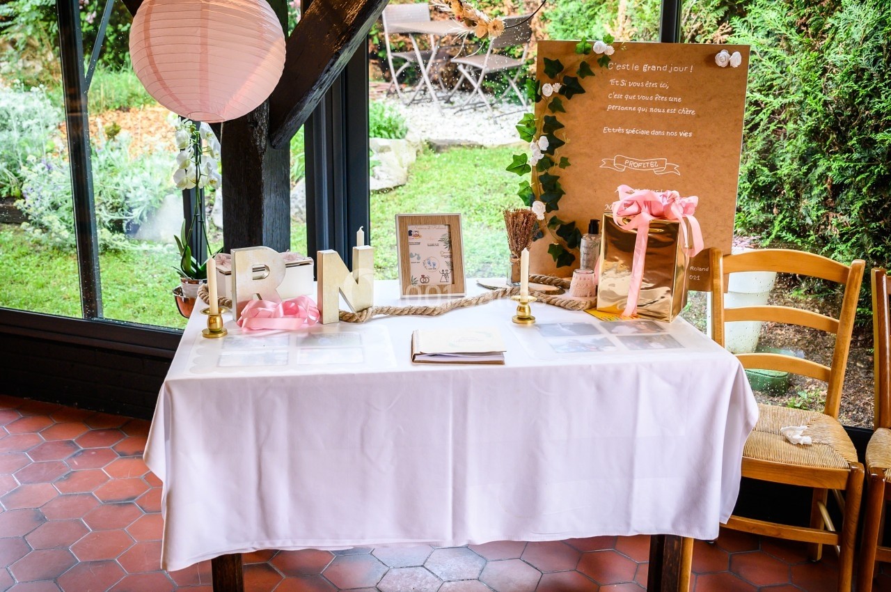 Location salle Bonneval (Eure-et-Loir) - Auberge de La Herse #21 Table décorée pour un mariage avec livre d'or, lettres dorées, lampion rose et panneau en carton dans un cadre verdoyant.