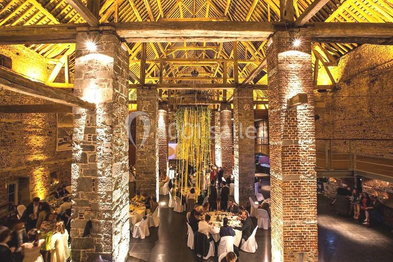 Location salle Anhée (Namur) - Ferme de l'Abbaye de Moulins #36 Salle en pierre et bois avec plafond voûté, éclairage chaleureux, tables dressées et invités lors d'un événement.