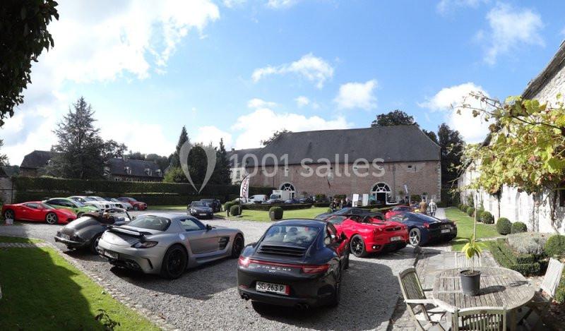 Location salle Anhée (Namur) - Ferme de l'Abbaye de Moulins #29 Plusieurs voitures de sport garées dans une cour pavée devant un bâtiment en briques avec un jardin environnant.